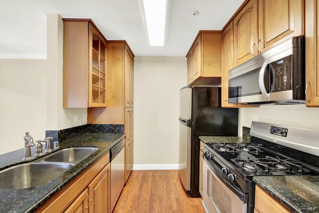 kitchen with dark stone counters, appliances with stainless steel finishes, a sink, and light wood-style floors