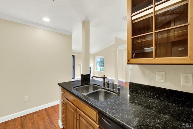 kitchen with a sink, dark stone counters, baseboards, wood finished floors, and brown cabinets