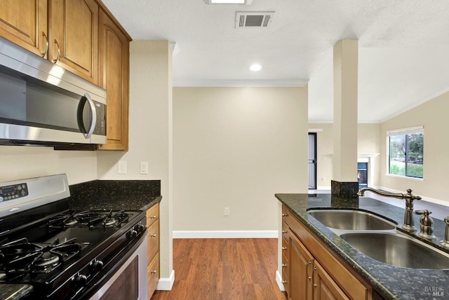 kitchen featuring visible vents, a sink, crown molding, brown cabinetry, and appliances with stainless steel finishes