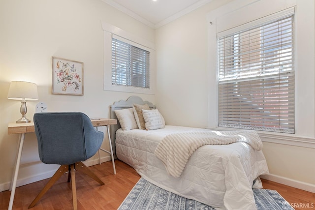 bedroom featuring baseboards, ornamental molding, wood finished floors, and multiple windows
