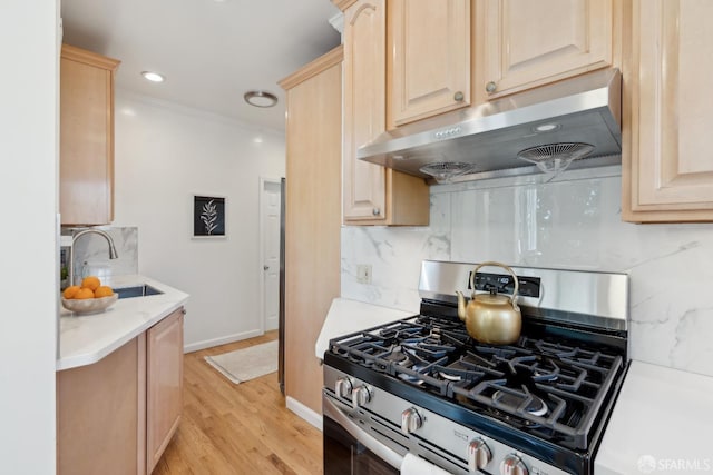 kitchen with stainless steel gas range, exhaust hood, a sink, and light brown cabinets