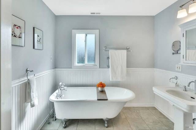 bathroom featuring wainscoting, a freestanding bath, tile patterned flooring, and a sink