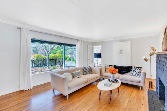 living area with a fireplace, light wood-style flooring, baseboards, and crown molding