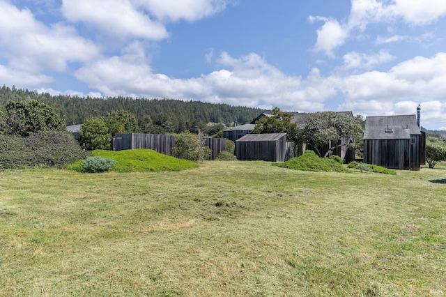 view of yard featuring an outbuilding, fence, and a wooded view