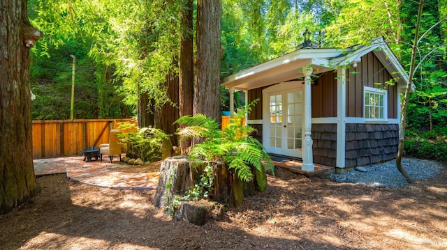 view of outbuilding with french doors, a forest view, fence, and an outdoor structure