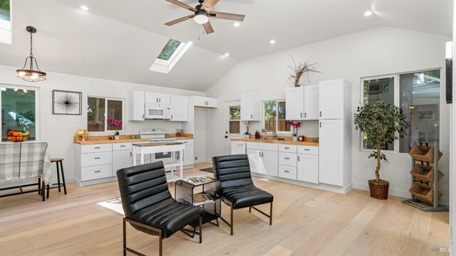 kitchen with vaulted ceiling with skylight, white appliances, a ceiling fan, white cabinets, and butcher block countertops