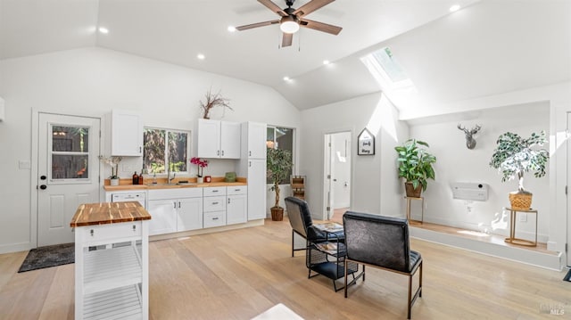 kitchen featuring wood counters, a ceiling fan, white cabinets, light wood-style floors, and lofted ceiling with skylight