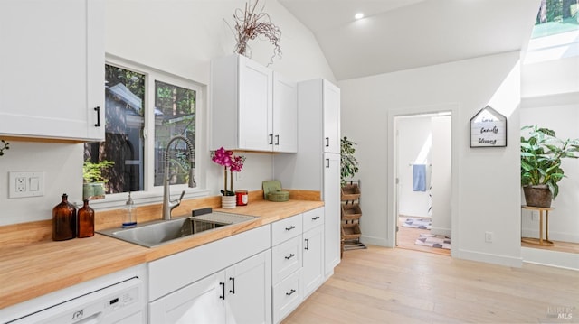 kitchen featuring light wood-type flooring, dishwasher, light countertops, a sink, and lofted ceiling