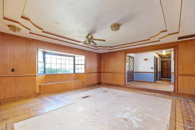 empty room with a raised ceiling, a textured ceiling, ceiling fan, and visible vents