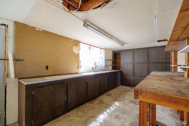 kitchen featuring open shelves, unfinished concrete flooring, and dark brown cabinets