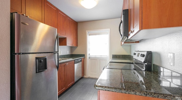 kitchen with dark stone counters, brown cabinets, dark wood-style floors, and stainless steel appliances