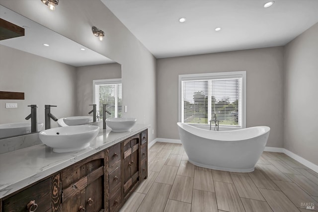 bathroom with double vanity, a sink, a freestanding tub, and baseboards