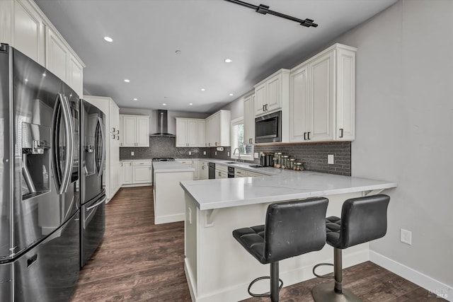 kitchen featuring black appliances, wall chimney exhaust hood, decorative backsplash, and a sink