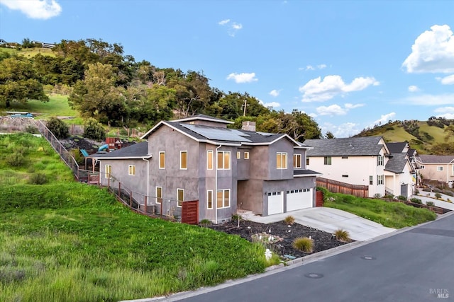 view of front of house featuring driveway, roof mounted solar panels, stucco siding, an attached garage, and fence