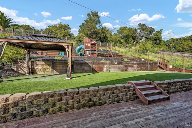 communal playground with fence, a wooden deck, and a lawn