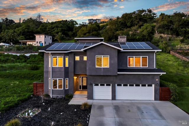modern home featuring a garage, stucco siding, roof mounted solar panels, and concrete driveway