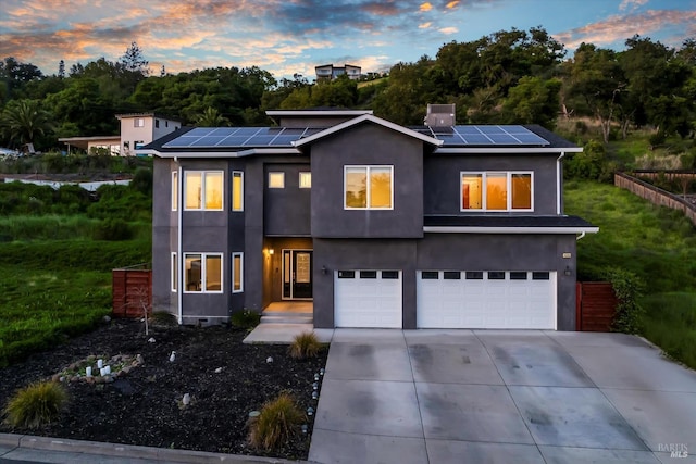 modern home with roof mounted solar panels, concrete driveway, stucco siding, and an attached garage