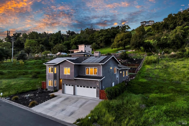 view of front of house featuring driveway, solar panels, an attached garage, and stucco siding