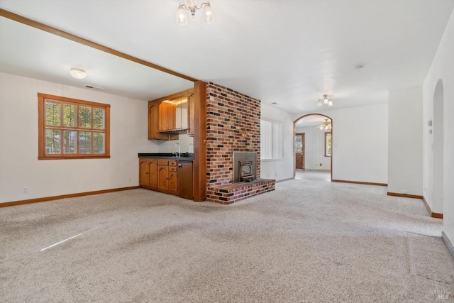 unfurnished living room with a sink, arched walkways, light colored carpet, baseboards, and visible vents