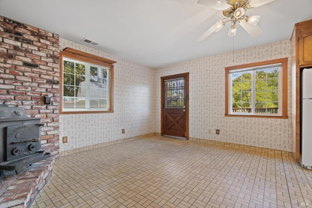 empty room featuring wallpapered walls, a wood stove, and brick patterned floor