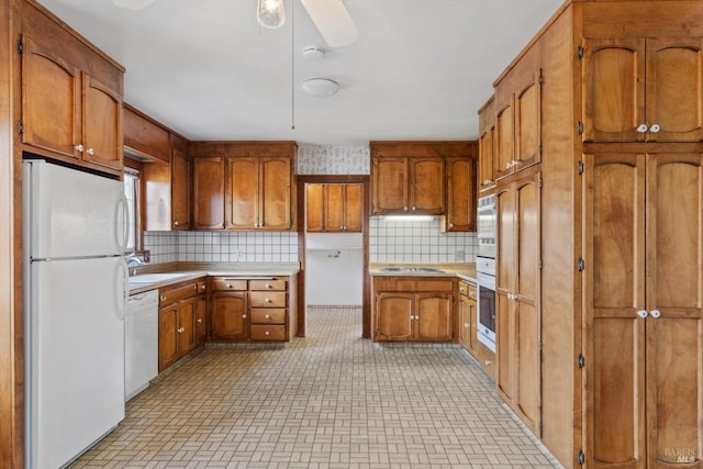 kitchen with tasteful backsplash, a sink, brown cabinetry, white appliances, and ceiling fan