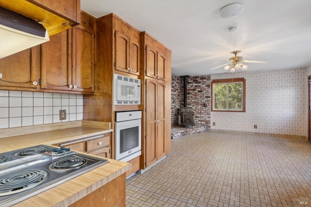 kitchen with brown cabinetry, a ceiling fan, a wood stove, and white appliances