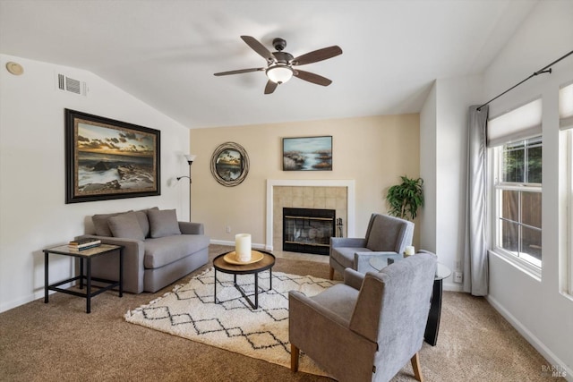 carpeted living room with a ceiling fan, vaulted ceiling, visible vents, a tiled fireplace, and baseboards
