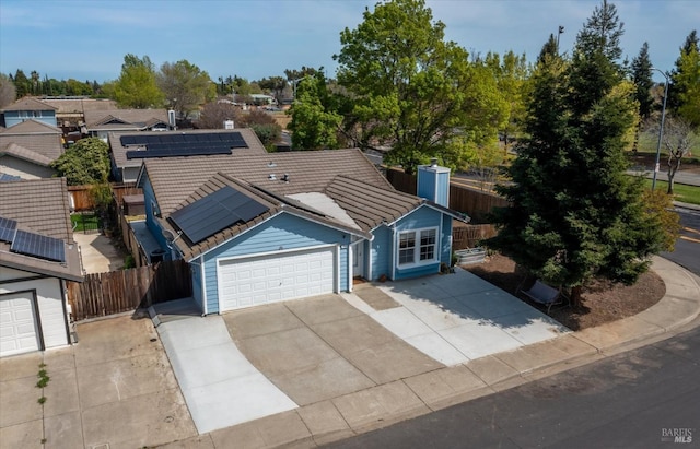 view of front of house featuring solar panels, an attached garage, a tile roof, fence, and driveway