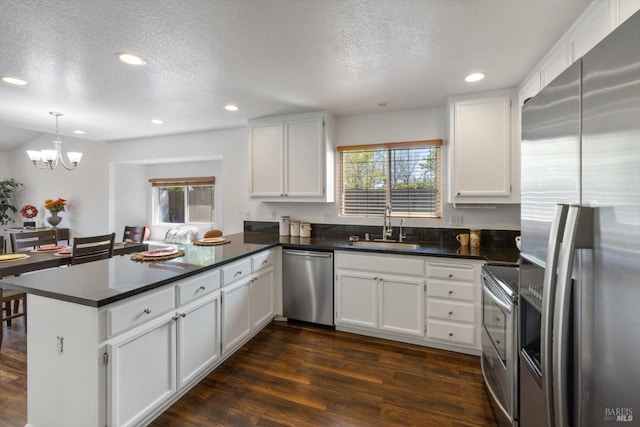 kitchen featuring dark countertops, a peninsula, a sink, and appliances with stainless steel finishes