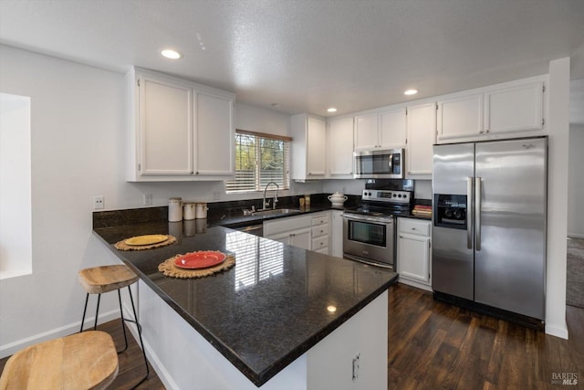 kitchen with stainless steel appliances, a peninsula, white cabinetry, and a sink
