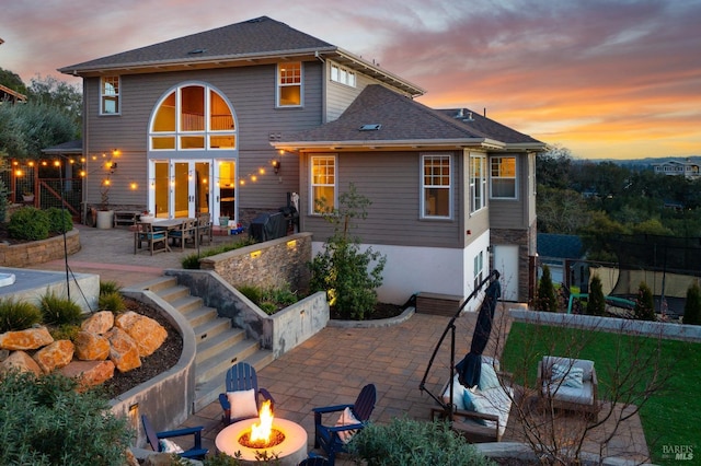 back of property at dusk with fence, a shingled roof, a fire pit, and a patio area