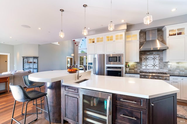 kitchen with a sink, wall chimney exhaust hood, stainless steel appliances, decorative backsplash, and wine cooler
