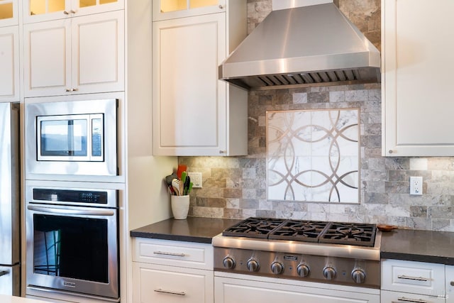 kitchen with dark countertops, wall chimney range hood, white cabinetry, tasteful backsplash, and stainless steel appliances