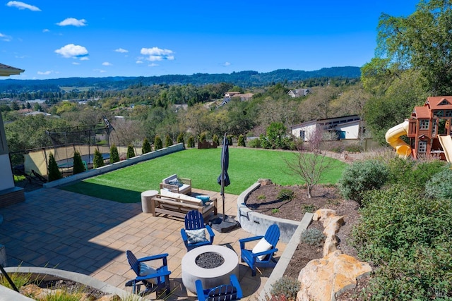 view of patio with a forest view, fence, a fire pit, and a playground
