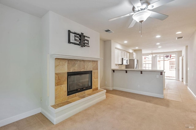 unfurnished living room with baseboards, a tiled fireplace, a ceiling fan, visible vents, and light colored carpet