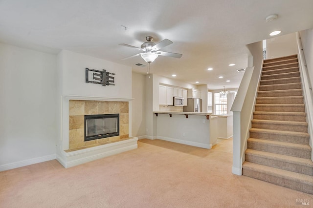 unfurnished living room featuring ceiling fan, light carpet, stairs, a tile fireplace, and baseboards