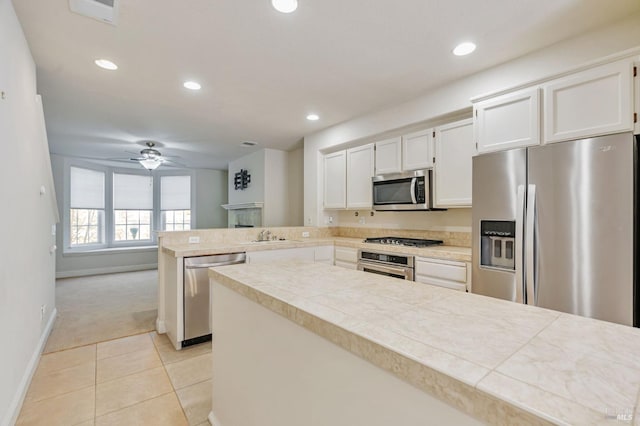 kitchen featuring ceiling fan, appliances with stainless steel finishes, a peninsula, white cabinetry, and light tile patterned flooring