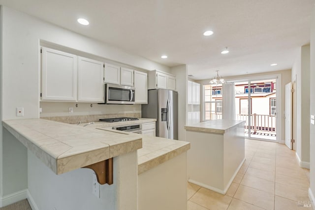 kitchen featuring white cabinets, a notable chandelier, a peninsula, stainless steel appliances, and a kitchen island
