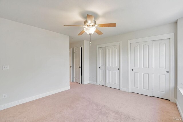 unfurnished bedroom featuring light carpet, baseboards, a ceiling fan, and multiple closets