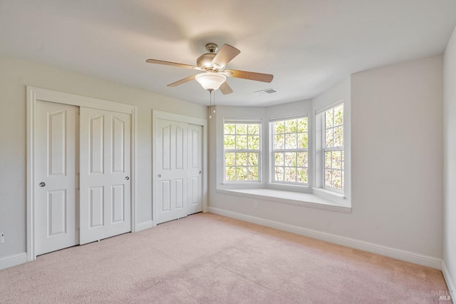 unfurnished bedroom featuring two closets, baseboards, carpet, and visible vents