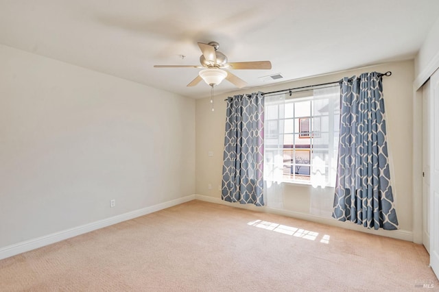 carpeted empty room with baseboards, a ceiling fan, and visible vents