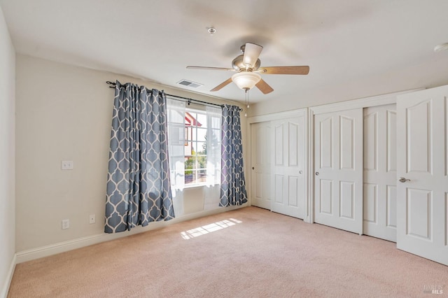 unfurnished bedroom with visible vents, baseboards, two closets, ceiling fan, and carpet