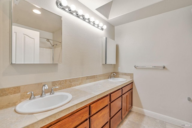 bathroom with a shower, double vanity, a sink, and baseboards