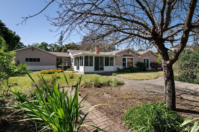 back of property featuring a lawn, a chimney, a sunroom, and stucco siding