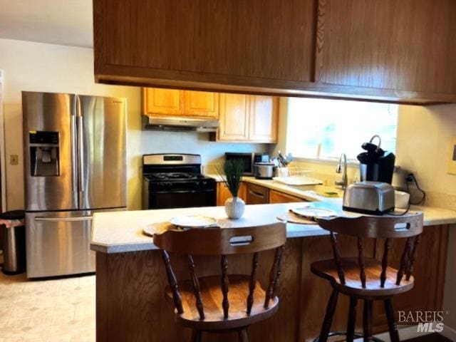 kitchen with stainless steel fridge with ice dispenser, a peninsula, under cabinet range hood, light countertops, and gas range oven