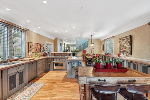 kitchen with light wood finished floors, a peninsula, a sink, oven, and recessed lighting