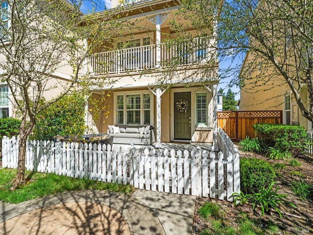 italianate home featuring covered porch, a balcony, and a fenced front yard