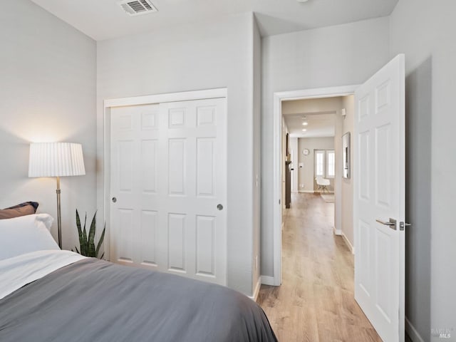 bedroom with baseboards, visible vents, a closet, and light wood finished floors