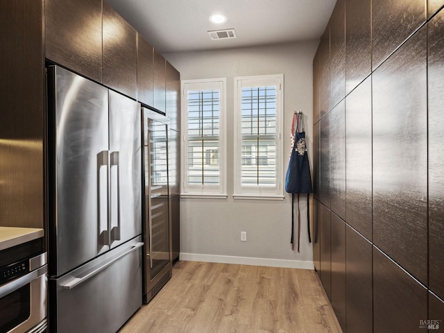 kitchen with appliances with stainless steel finishes, visible vents, baseboards, dark brown cabinetry, and light wood-type flooring