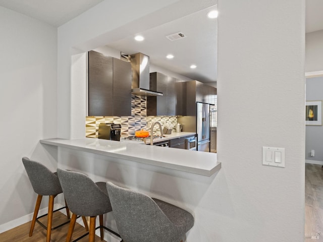 kitchen with wall chimney range hood, visible vents, tasteful backsplash, and light countertops